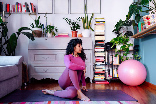Woman practicing yoga at home sitting on mat in ardha matsyendrasana pose