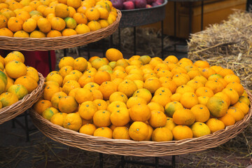 Baskets filled with fresh oranges displayed at a market stall, surrounded by rustic straw decorations, evoking a natural and vibrant countryside setting