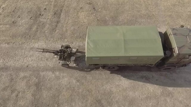 Air defense, anti-aircraft gun. Military truck carries a ZU-23-2 anti-aircraft gun on a trailer. View from above. Aerial view, drone follows a military truck. Soviet-style anti-aircraft gun ZU23
