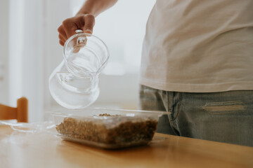 A young man waters wheat seeds into a container.