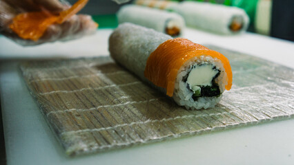 The chef places slices of salmon on a rice roll. Cream cheese inside. Preparing a Philadelphia roll. Cloud kitchen. Close up.