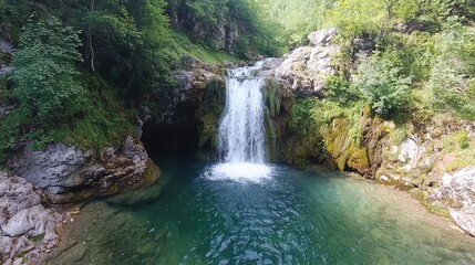 Fototapeta premium Waterfall cascading into a pool in a lush green forest; aerial view, perfect for travel brochures