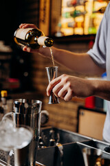 Bartender pouring liquor into a jigger, preparing a crafted cocktail in a modern bar setting