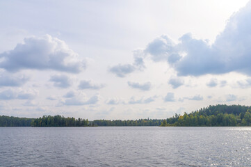 White fluffy clouds, sun and bright sky over the surface of the lake. Majestic view.