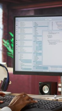 Vertical video Engineer in home office looks at UI on computer monitor, typing and executing programming code. Panning shot of IT worker using coding application to write and test code in modern