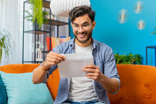 Happy Indian Hindu man open envelope letter, reading it. Career growth advance promotion, bank loan approve, successful admission to university monetary award invitation great news, lottery game win