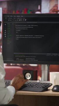Vertical video IT technician in home office looking at UI on computer monitor, executing programming script. Remote employee using coding application to write and test code in modern apartment, camera