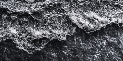 A serene black and white photo of the ocean with waves and foam