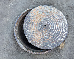 Open manhole with textured cover on a concrete surface
