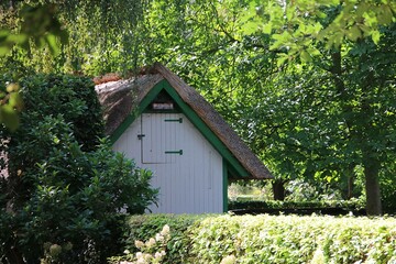 pretty little white thatched garden house is hidden behind a hedge in the garden