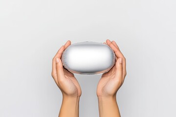 Hands holding a sleek, silver oval object against a plain white background, suggesting modern design