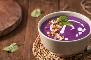 Healthy creamy red cabbage soup topped with herbs, a swirl of cream, toasted almonds, and fresh herbs, resting on a rustic wooden board.