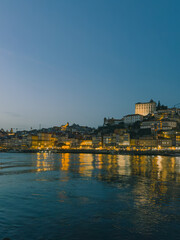 Fototapeta premium A serene sunset casts a warm glow over the Douro River, highlighting the historic architecture of Porto, Portugal.