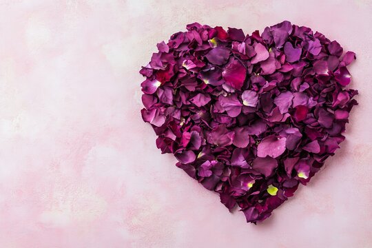 A red paper heart that has been split into halves against a light pastel pink background. The composition symbolizes a broken heart, captured from a top-down perspective.