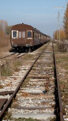 Fototapeta premium Rusty railcar abandoned on overgrown tracks under a clear sky, highlighting a mix of neglect and the beauty of nature reclaiming the area