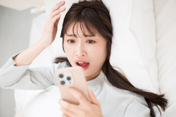 寝坊してベッドでスマホで時間をみる女性　遅刻だ～
