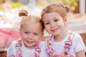 Two preschooler sisters happily sitting together outdoors in kindergarten yard