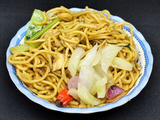 Fried noodles with soy sauce served with pickles, chili, vegetables and meat. Fried noodles with black background.