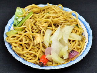 Fried noodles with soy sauce served with pickles, chili, vegetables and meat. Fried noodles with black background.