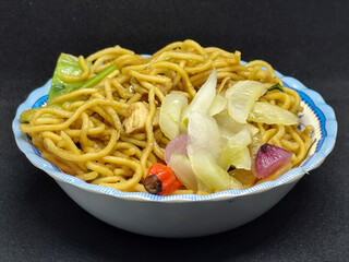 Fried noodles with soy sauce served with pickles, chili, vegetables and meat. Fried noodles with black background.