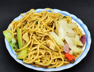 Fried noodles with soy sauce served with pickles, chili, vegetables and meat. Fried noodles with black background.