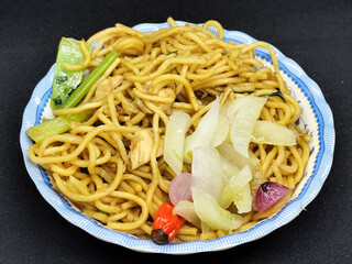 Fried noodles with soy sauce served with pickles, chili, vegetables and meat. Fried noodles with black background.