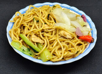 Fried noodles with soy sauce served with pickles, chili, vegetables and meat. Fried noodles with black background.