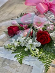 A beautifully arranged flower bouquet featuring red roses, white blooms, pink gerberas, lush greenery, and a pink ribbon, suitable for gifting on special occasions or celebrations.