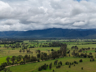 Obraz premium Aerial View of Lush Green Pastures and Wooded Fields with Mountain Range in the Background 