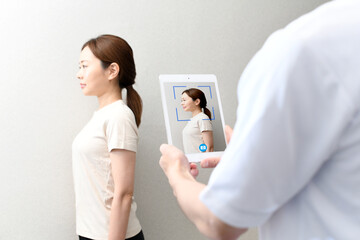 タブレット端末で女性患者を撮影する整体師
