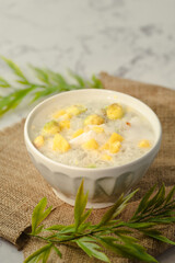 A white bowl of soup with yellow and green pieces of food in it