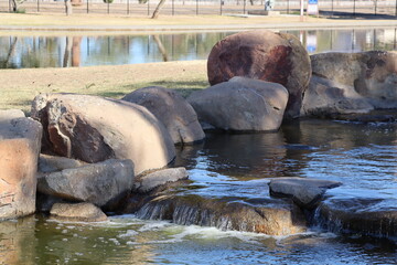 Fototapeta premium Boulder and rocks guarding a manmade cozy little waterfall at recreational Cortez park lake in Phoenix, Arizona in winter