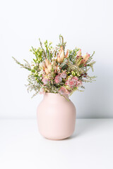 A beautiful floral arrangement blushing bride protea, eucalyptus leaves, wax flowers and delicate thryptomene flowers. In a stylish pink ceramic vase, with a white background.
