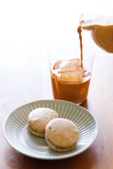 Thai iced tea. Cold drink from Ceylon black tea and milk pouring over ice. Brown orange Ceylon black tea flavor macaron on wooden table.