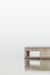 Obraz premium Serene concrete pier extending into misty calm waters at sunrise