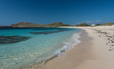 Fototapeta premium Secluded white sand beach with crystal clear turquoise water and distant hills under a blue sky.