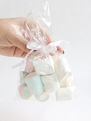 A woman's hand holds a transparent bag with marshmallows on a white background. A sweet gift. Sugar colored marshmallows.