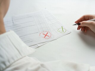 A woman in a white shirt is sitting at a table in an office, on the table are documents with a refusal and a green check mark. Drawing up a contract. Refusal and consent, choice. Controversial issues. © Ira