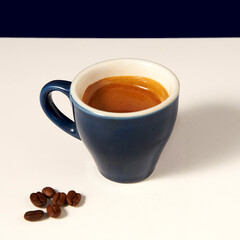 A glass of black coffee with coffee crema on top of it, in a blue coffee mug ,on a white and dark blue background                                                                      