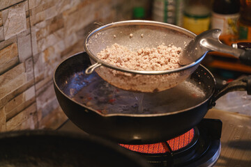 Straining cooked minced meat over a boiling pot on a kitchen stove.