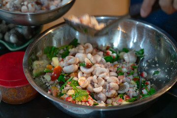 A vibrant mix of fresh clams, vegetables, and herbs in a stainless steel bowl, ready for preparation of a seafood dish.