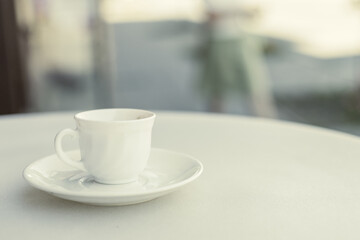 a white coffee cup and saucer on a white table outside the room