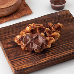 A fusion of croissant and waffle, called croffle, with chocolate sauce and toppings, in a white...