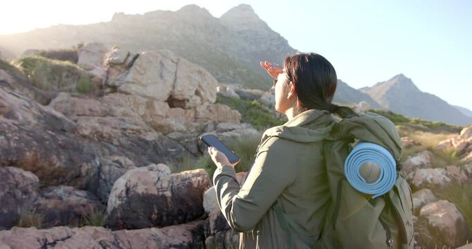 Hiking in mountains, woman with backpack holding smartphone and looking ahead