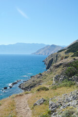 Fototapeta premium A hiking trail winds along the western edge of Baska Bay in Croatia, offering picturesque views of the Adriatic Sea and the surrounding rocky landscape