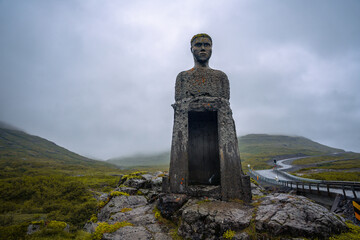 Journey through Iceland's Westfjords, where a roadside statue adds charm to the cloudy mountain backdrop of this rugged region
