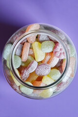 A glass jar full of colorful fruit candies on a purple background