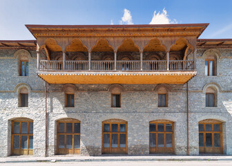 The Lower Caravanserai in Shaki, Azerbaijan features intricate stonework and ornate wooden big balcony, highlighting traditional design under sunny skies