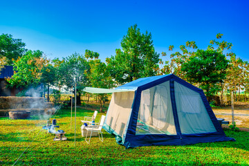 Camping tents on green grass  in the morning, vintage cabin tents, antique gas lamps, retro chairs,  with outdoor coffee-making facilities on  tables in a forest camping area forest
