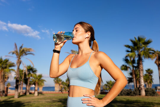 Fit woman drinking water after working out in a park with palm trees